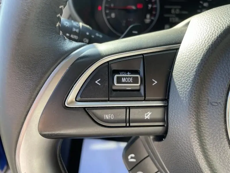 Gros plan sur les commandes au volant côté gauche d’une Suzuki Swift 2024 bleu métal, boutons mode et volume visibles.