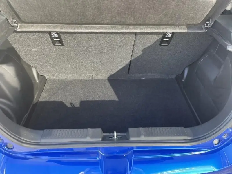 Coffre ouvert vu de l'arrière d'une Suzuki Swift 2024 bleu métal, montrant l'espace de chargement vide et la moquette noire.
