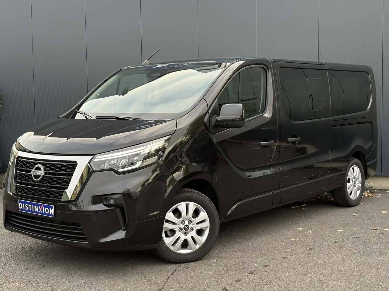 Nissan Primastar Combi noir métal vu en 3/4 avant droit avec hayon arrière vitré et jantes alliage 17 pouces.