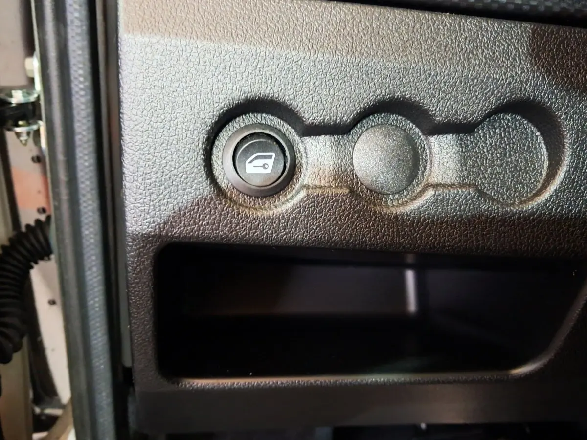 Détail intérieur montrant le bouton d'ouverture du coffre sur la portière côté conducteur d'une Aixam Ambition blanche.