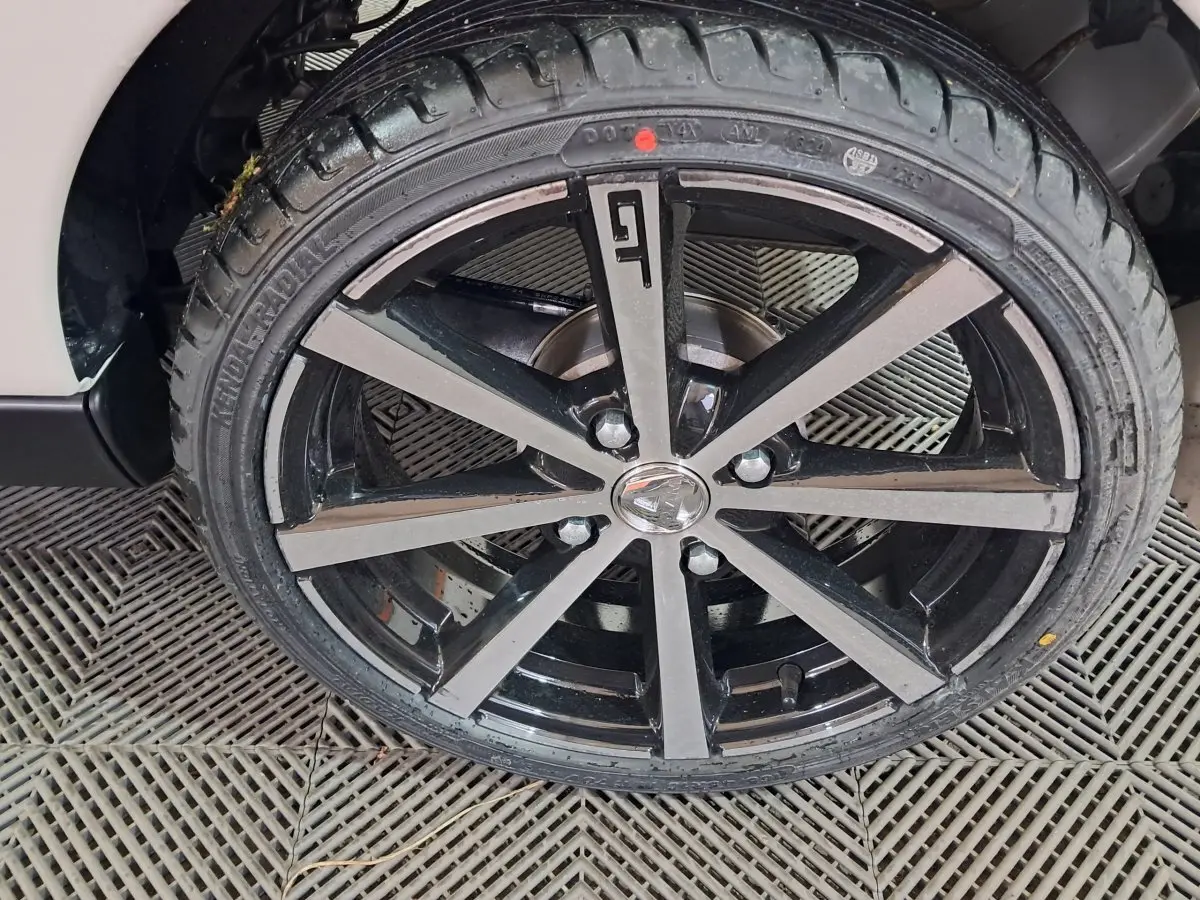 Gros plan sur la jante noire et grise avec logo GT de l'AIXAM AMBITION 0.5 CITY COUPE GTI blanche, côté roue avant.