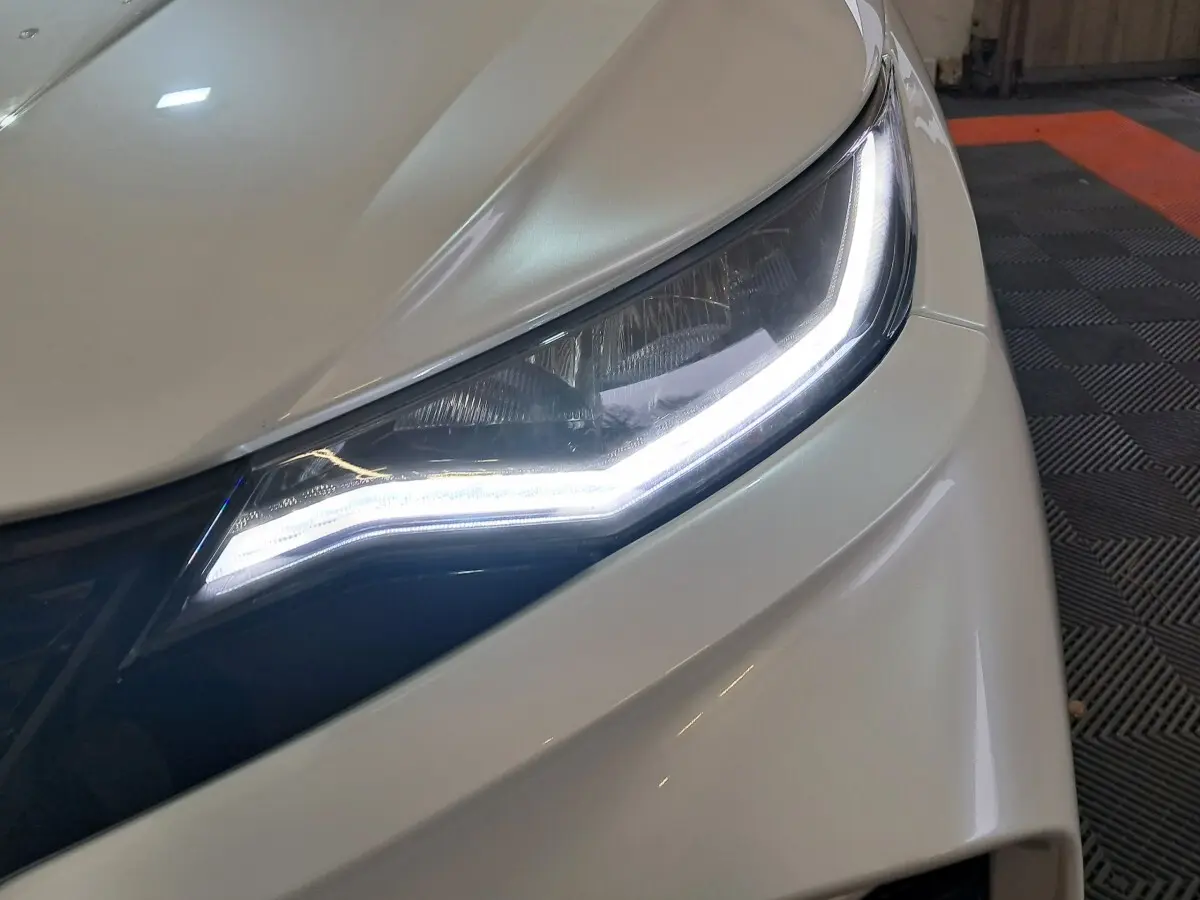 Gros plan sur le phare avant droit blanc d'une Aixam Ambition 0.5 City Coupe GTI 2026 avec éclairage LED allumé.