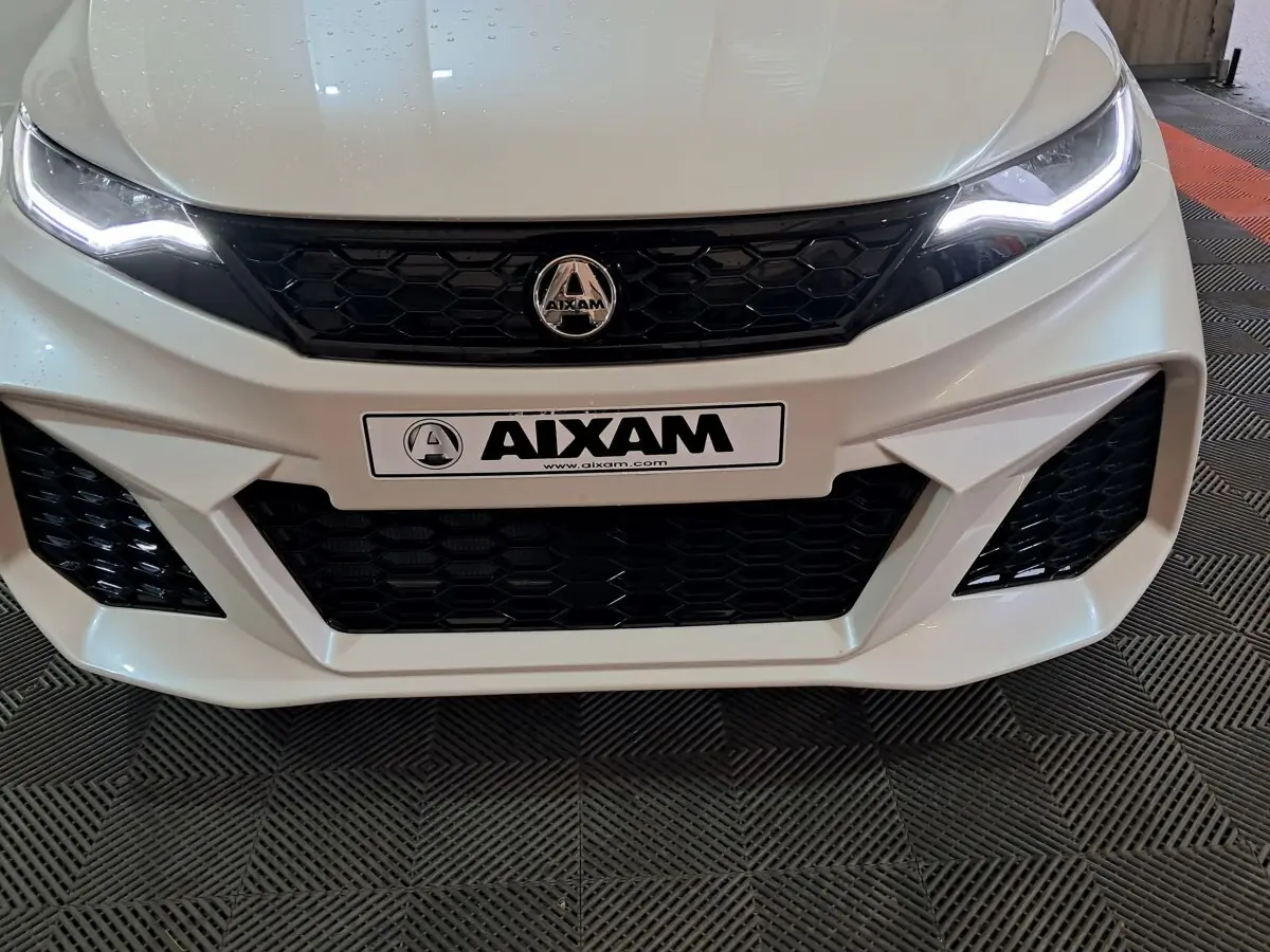 Vue frontale rapprochée de l'AIXAM AMBITION 0.5 CITY COUPE GTI blanche avec calandre noire et phares LED allumés.