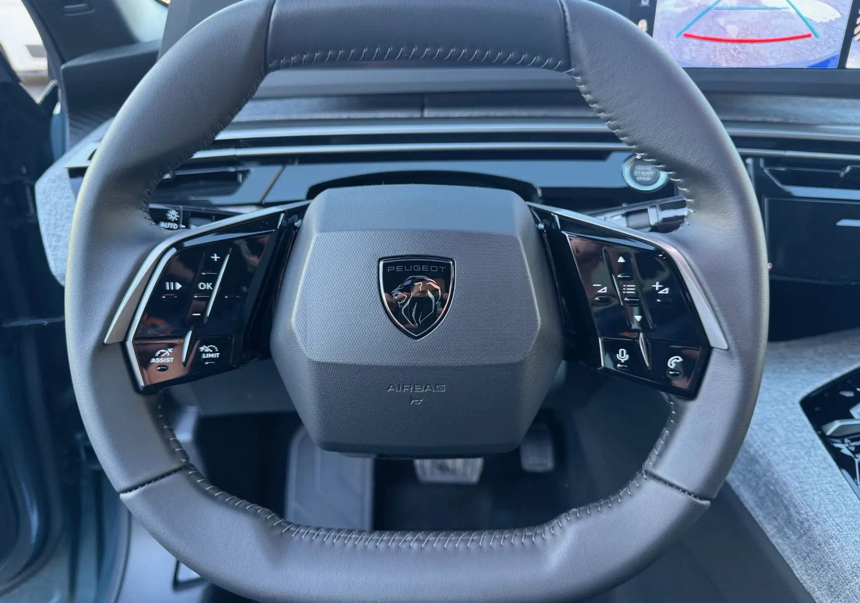 Vue rapprochée du volant cuir noir du Peugeot 3008 Hybrid 2025 avec commandes intégrées et écran de recul visible.