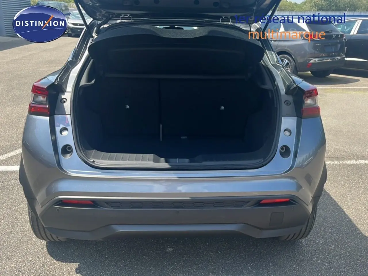 Vue arrière d’un Nissan Juke Hybrid gris squale métal avec coffre ouvert, soulignant son espace de chargement.