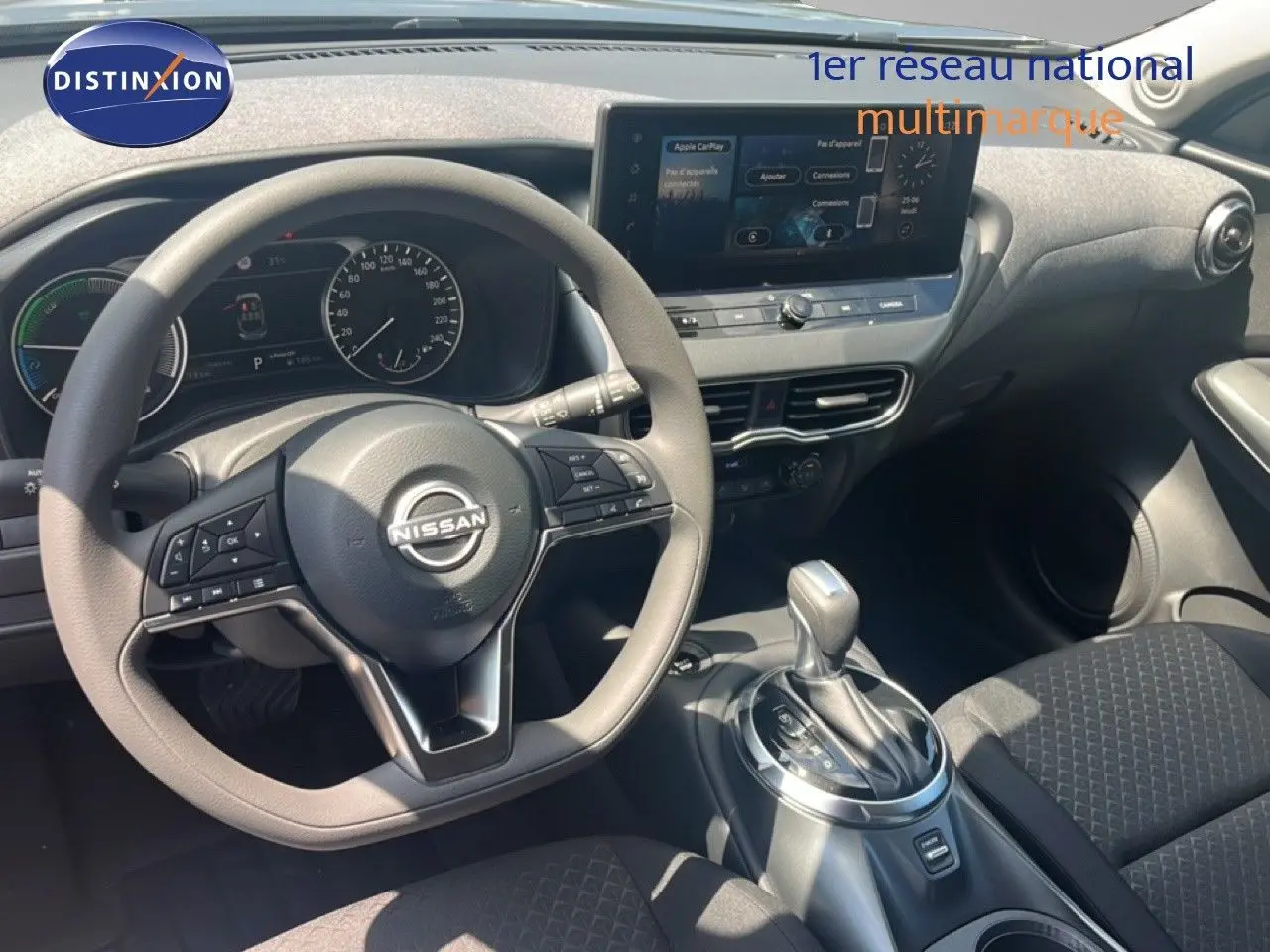 Vue intérieure du poste de conduite du Nissan Juke Hybrid 2025, volant multifonction et écran tactile central visibles.