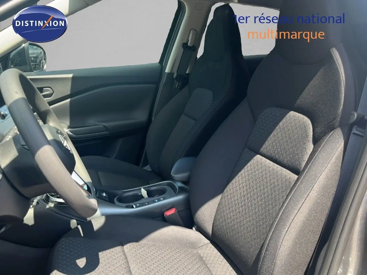 Vue intérieure côté conducteur du Nissan Juke Hybrid 2025, sièges tissu gris et volant multifonction.