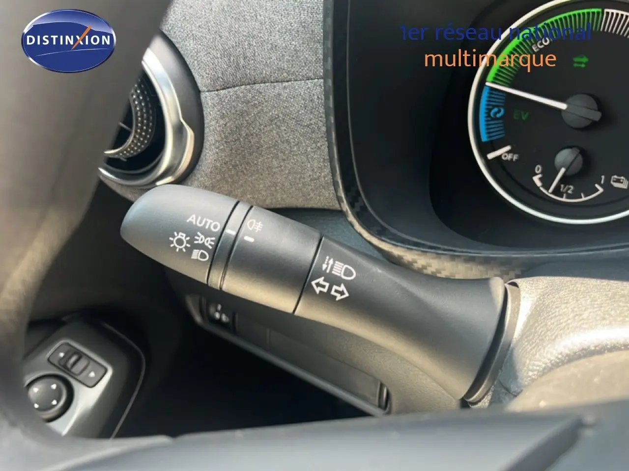 Gros plan sur la commande des feux et clignotants à gauche du volant du Nissan Juke hybride gris, avec tableau de bord partiel visible.