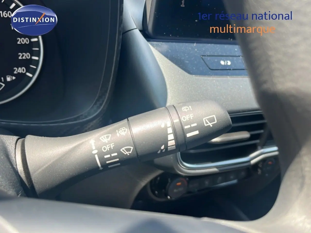Gros plan sur la commande d’essuie-glace à gauche du volant du Nissan Juke gris, avec tableau de bord et écran tactile en arrière-plan.