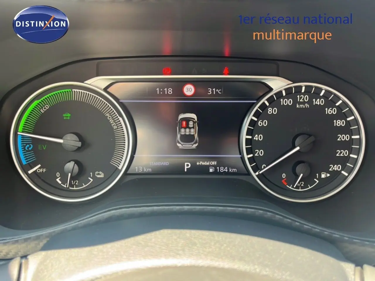 Vue rapprochée du tableau de bord numérique du Nissan Juke Hybrid gris, affichant la vitesse, autonomie et indicateurs hybrides.