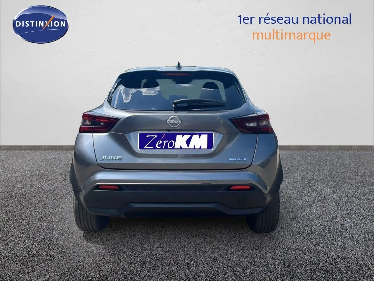 Vue arrière d'un Nissan Juke gris squale métal 2025 avec logo Hybrid et plaque Zéro KM visible sur fond neutre.
