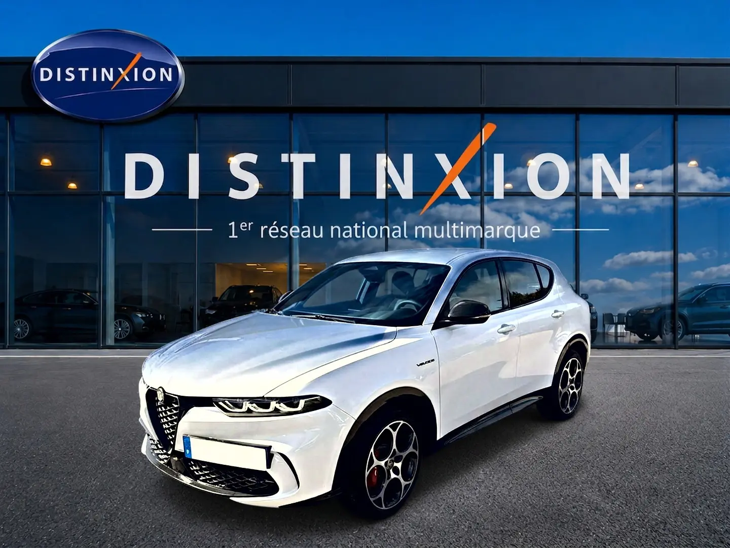 Vue 3/4 avant d'une Alfa Romeo Tonale blanche avec jantes spécifiques et calandre caractéristique, devant une vitrine Distinxion.