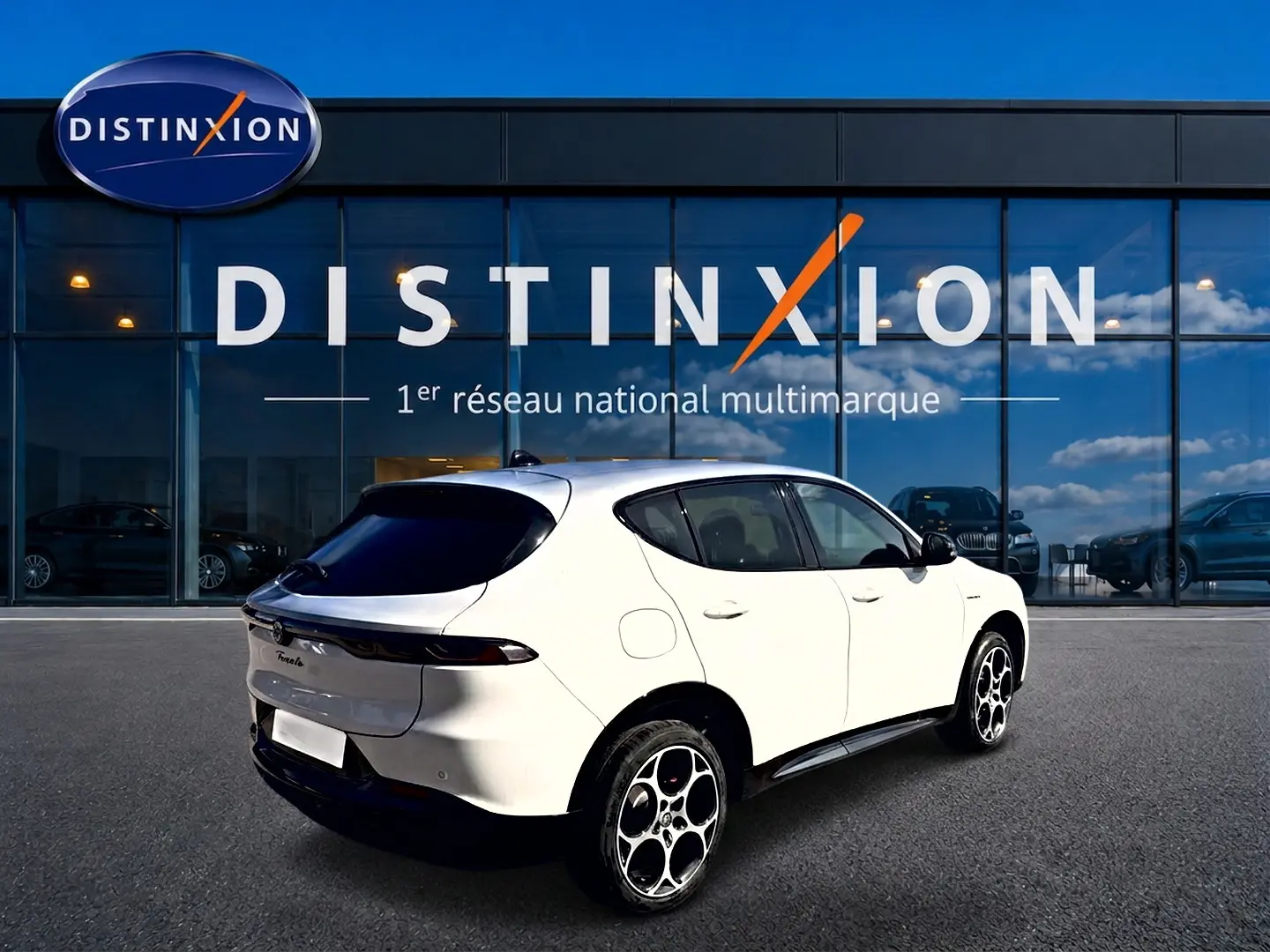 Vue 3/4 arrière droite d'un Alfa Romeo Tonale blanc avec jantes alu distinctives, stationné devant un showroom Distinxion.