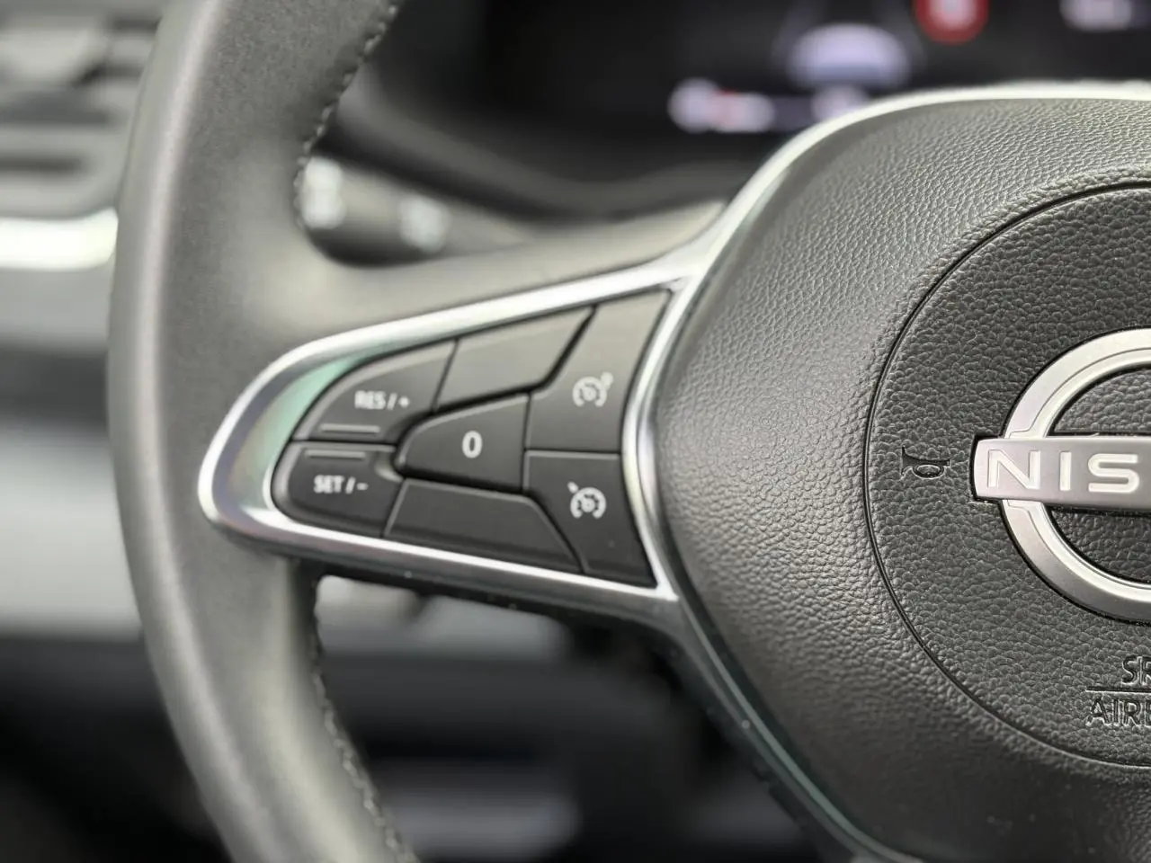 Gros plan sur les commandes au volant noir du Nissan Primastar Combi 2025, soulignant le logo central et les boutons de régulateur.
