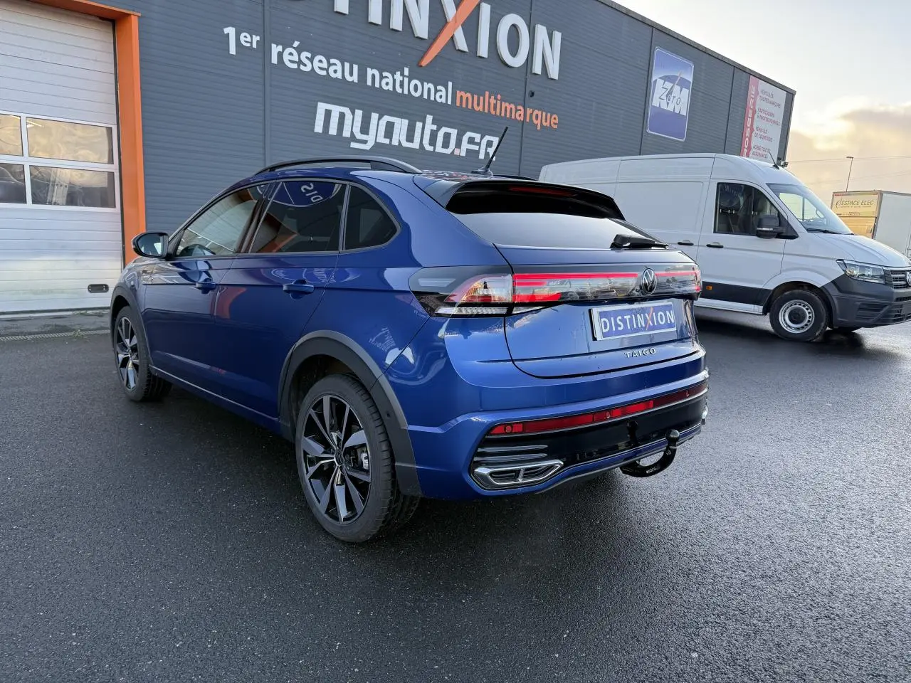 Vue 3/4 arrière droite du Volkswagen Taigo bleu récif métallisé avec jantes noires brillantes et attelage amovible.
