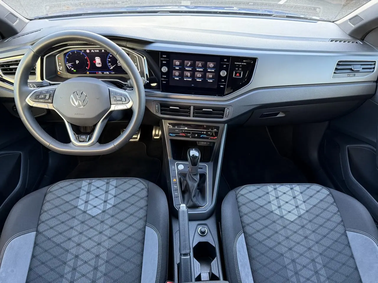 Vue intérieure avant du Volkswagen Taigo 2025, tableau de bord moderne avec écran tactile et sièges tissu gris à motifs géométriques.