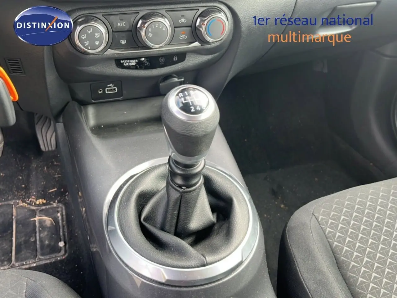 Gros plan sur la console centrale du Nissan Juke 2023 noir métal, avec levier de vitesse manuel et commandes de climatisation.