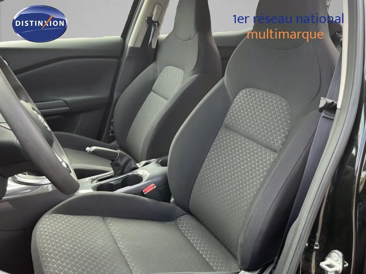 Vue intérieure côté conducteur du Nissan Juke 2023 montrant les sièges en tissu gris et la console centrale noire.
