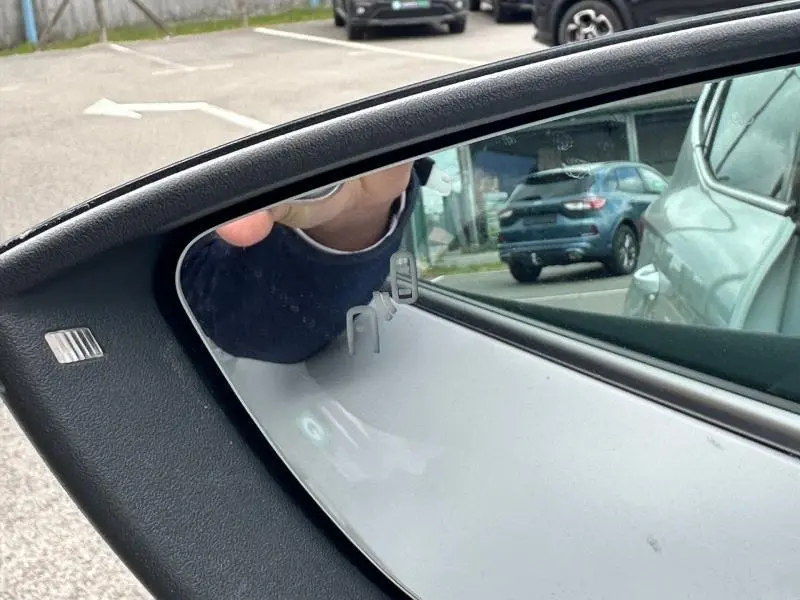 Gros plan sur le rétroviseur côté gauche du SEAT Arona blanc Nevada avec toit noir, reflet du parking visible.