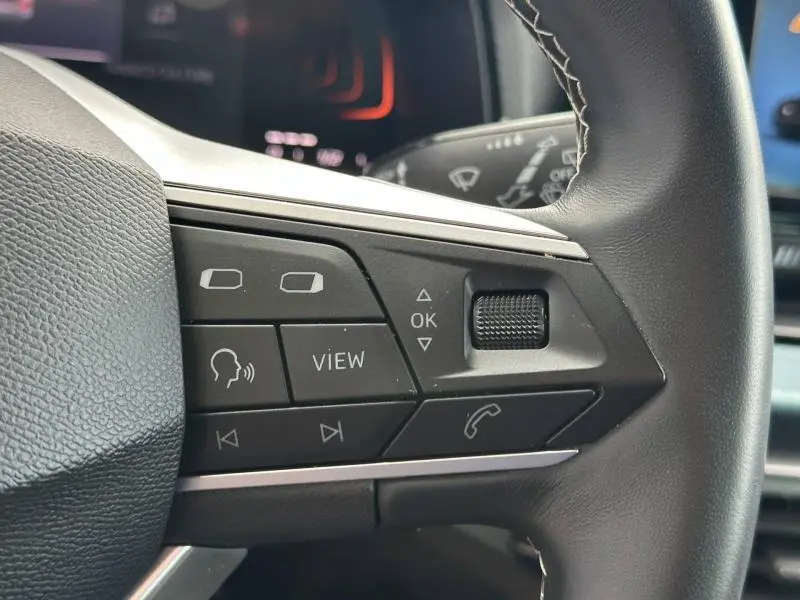 Gros plan sur les commandes multifonctions noires du volant cuir du SEAT Arona blanc, avec boutons de navigation et appel.