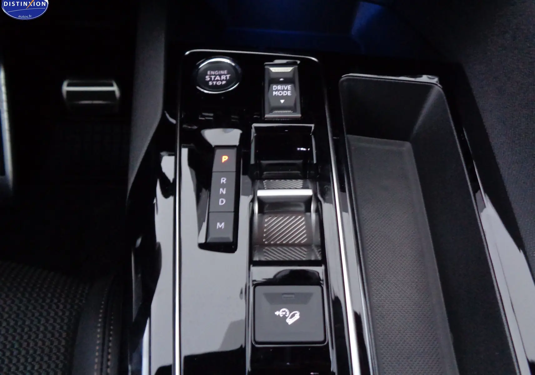 Gros plan sur la console centrale noire brillante du Peugeot 3008 2023 avec bouton start, levier de vitesses et commandes de conduite.