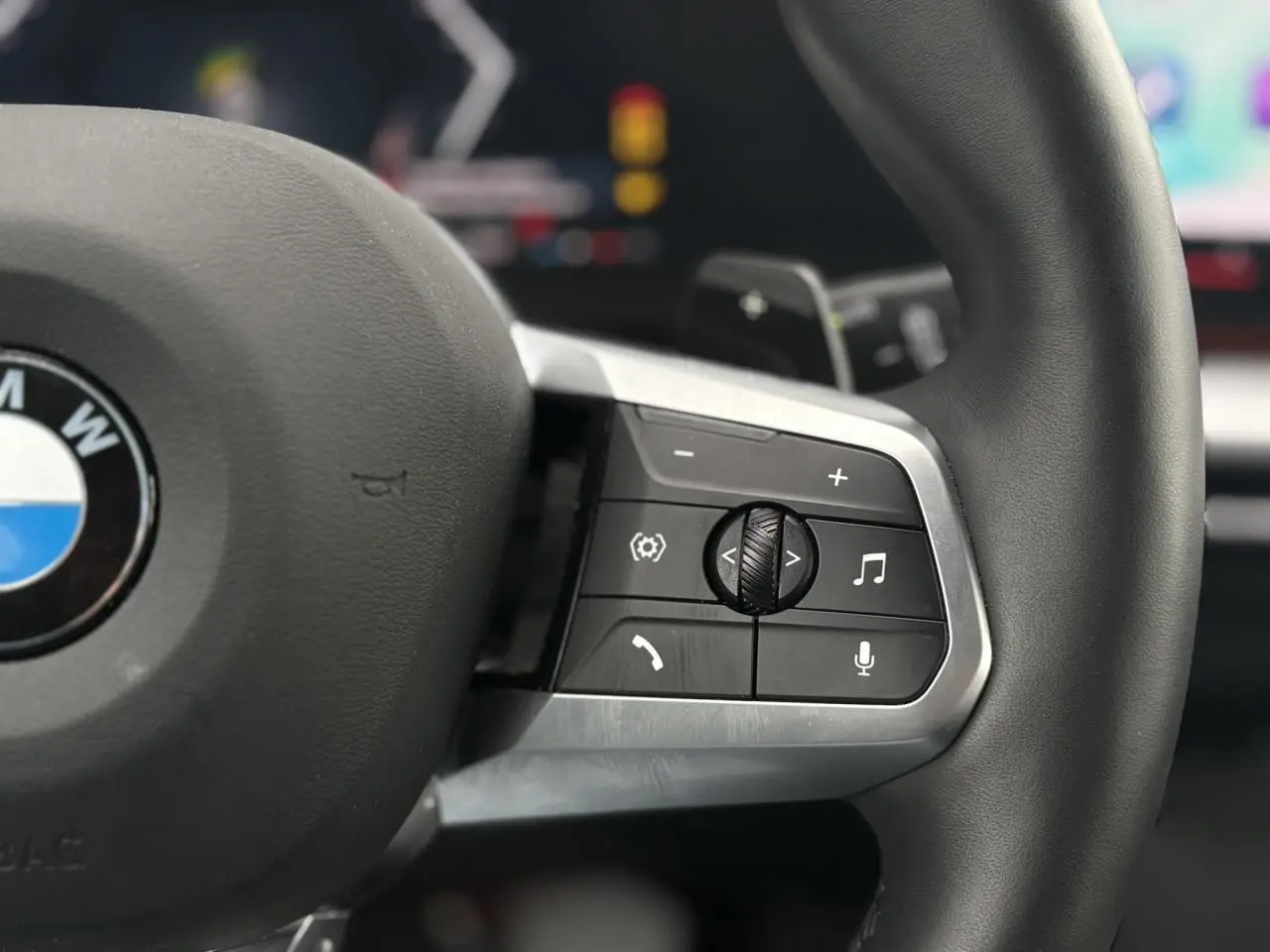 Gros plan sur les commandes multifonctions à droite du volant cuir noir du BMW X1 blanc Mineral 2025.