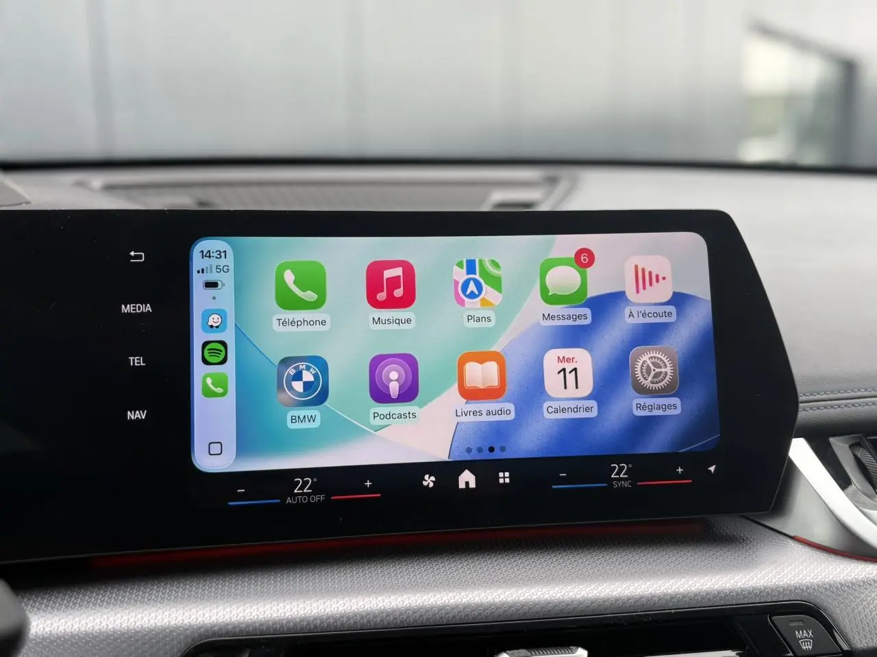 Écran tactile incurvé du tableau de bord du BMW X1 blanc Mineral, affichant l'interface Apple CarPlay.