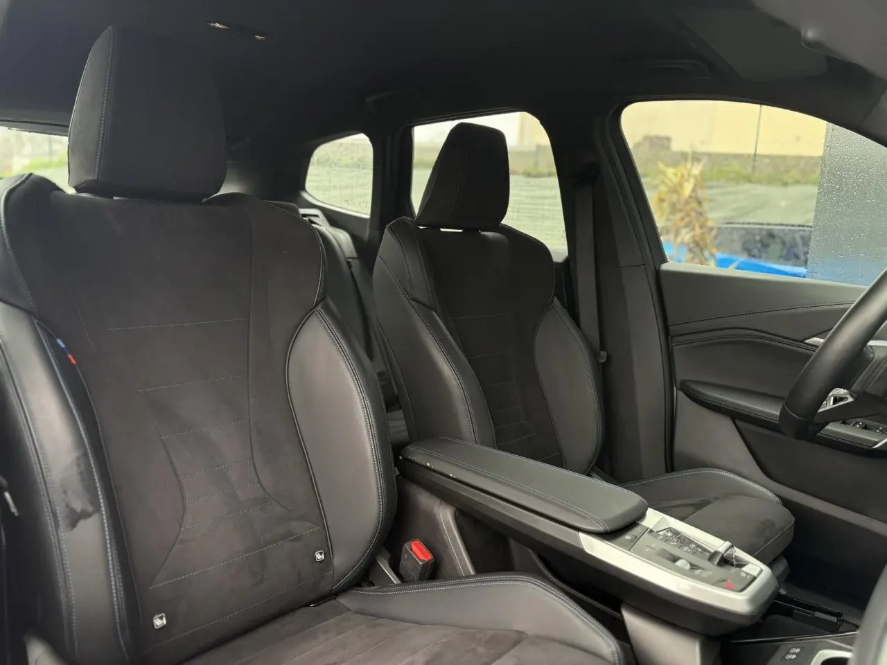 Vue intérieure côté droit montrant les sièges avant sport en Alcantara noir avec surpiqûres bleues du BMW X1 2025.