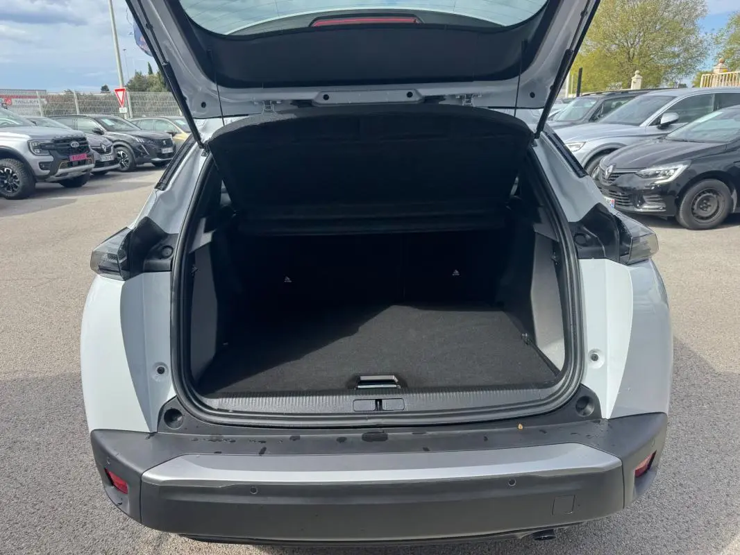 Coffre ouvert vu de l'arrière d'un Peugeot 2008 blanc 2024 avec barres de toit et jantes alliage 17 pouces.