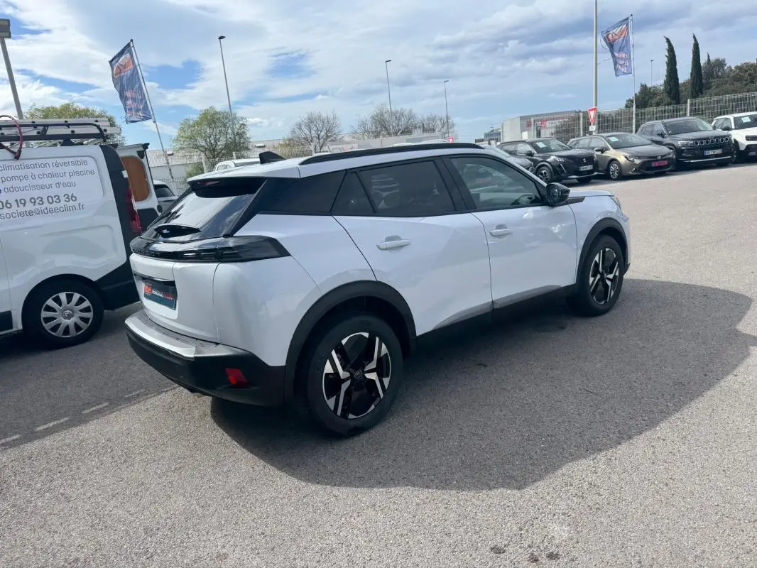 Peugeot 2008 blanc vue 3/4 arrière droit avec barres de toit et jantes alliage 17 pouces sur parking.