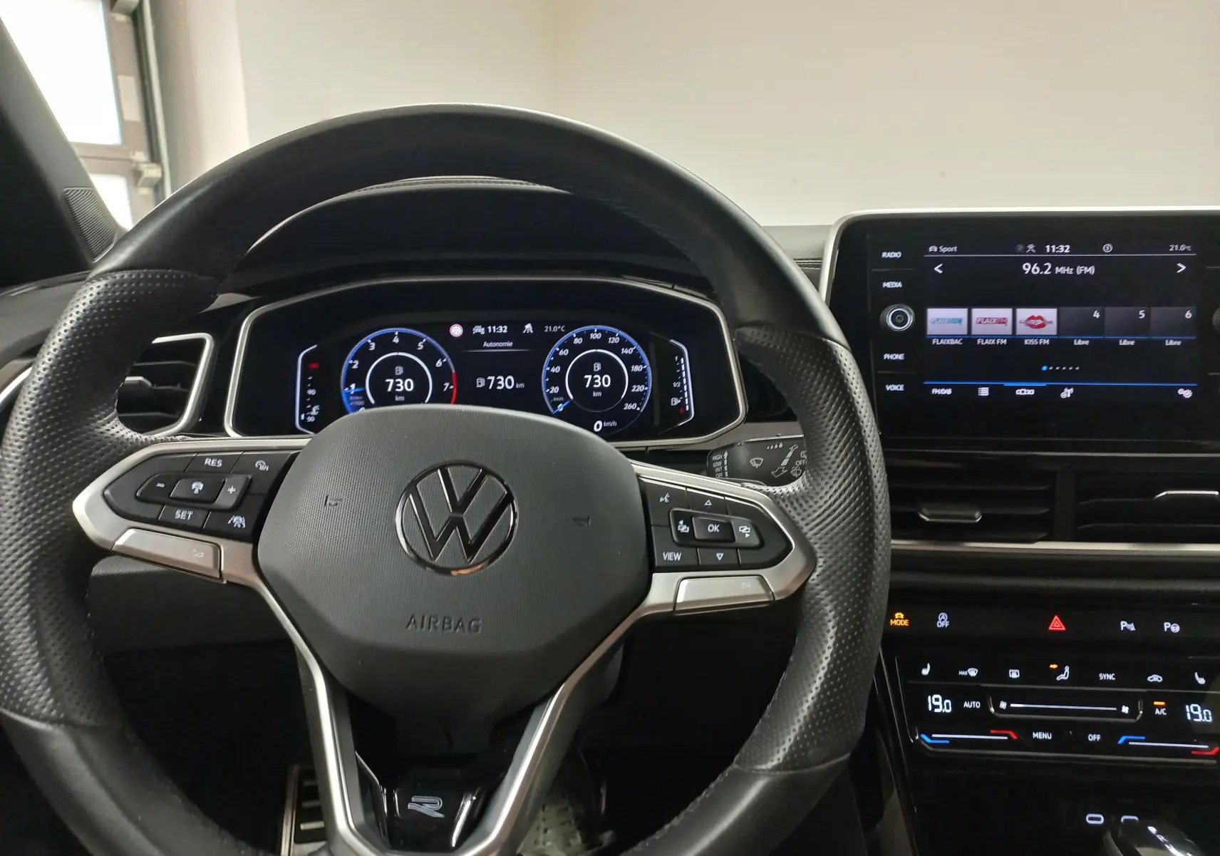 Vue intérieure centrée sur le volant multifonction noir du Volkswagen T-Roc 1.5 TSI R-Line avec tableau de bord digital et écran tactile.