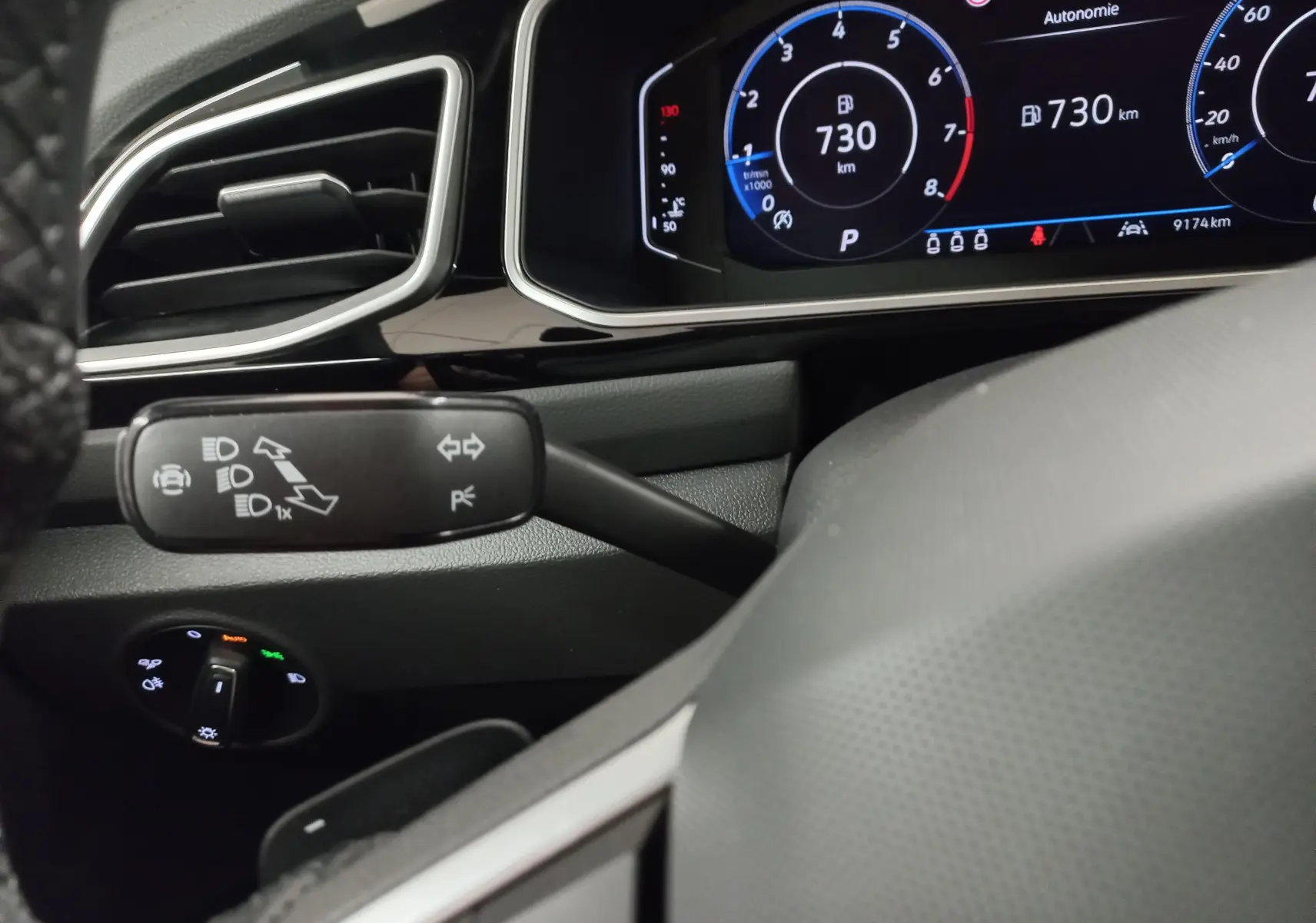 Gros plan intérieur sur le combiné d'instruments numérique et la commande des feux du Volkswagen T-Roc 1.5 TSI noir intense nacré.