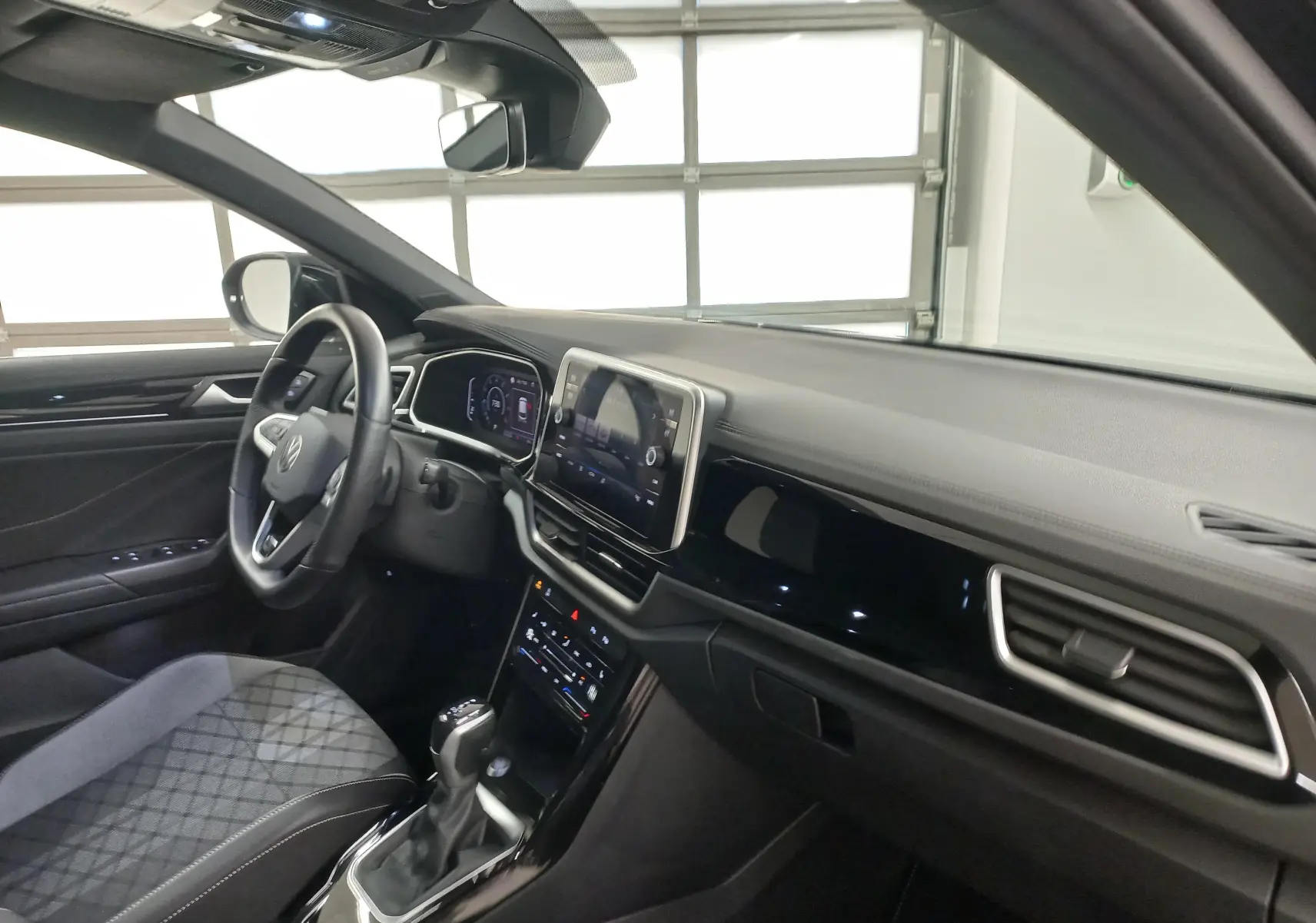 Vue intérieure côté conducteur du Volkswagen T-Roc 1.5 TSI 2025, tableau de bord noir avec écran tactile central.
