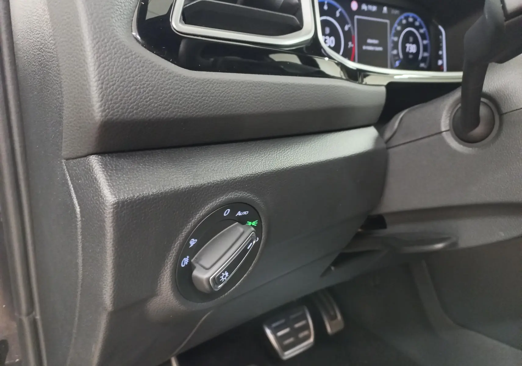 Détail du tableau de bord côté gauche du Volkswagen T-Roc 2025 noir intense, avec commande des phares et pédales en aluminium.