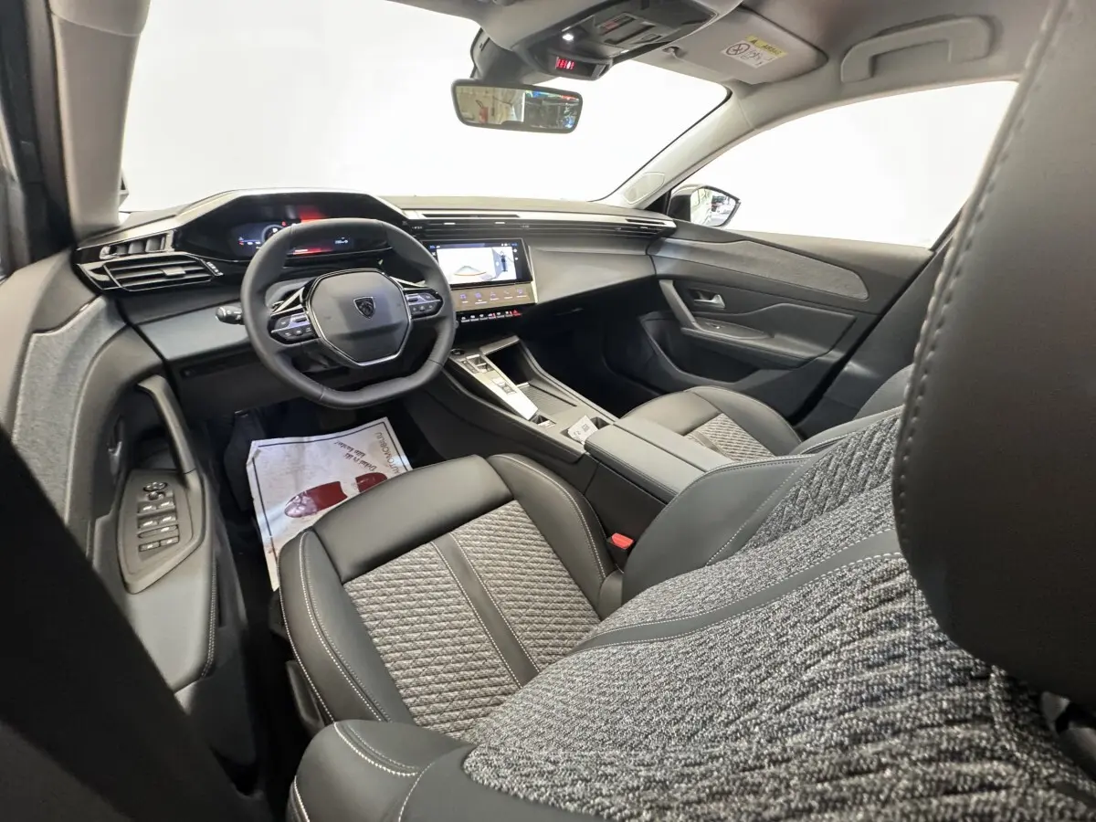 Intérieur de la Peugeot 308 2026 vu côté conducteur, sièges cuir et tissu gris, tableau de bord avec écran tactile.