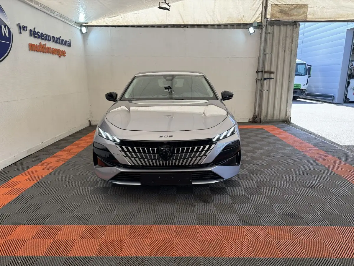 Peugeot 308 BlueHDi 130 gris clair vue de face, mettant en valeur sa calandre distinctive et ses phares LED fins.