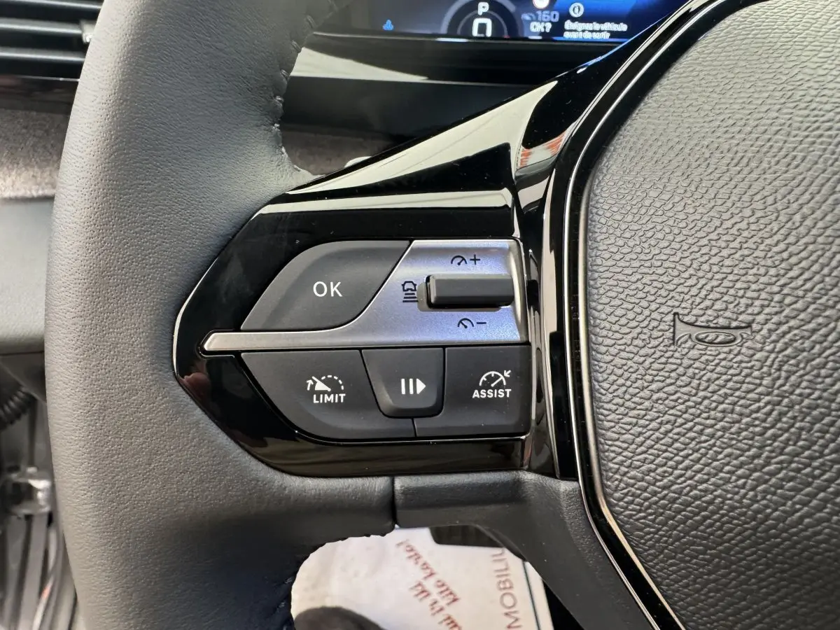 Gros plan sur le volant cuir gris de la Peugeot 308 2026, avec commandes multifonctions et régulateur adaptatif.