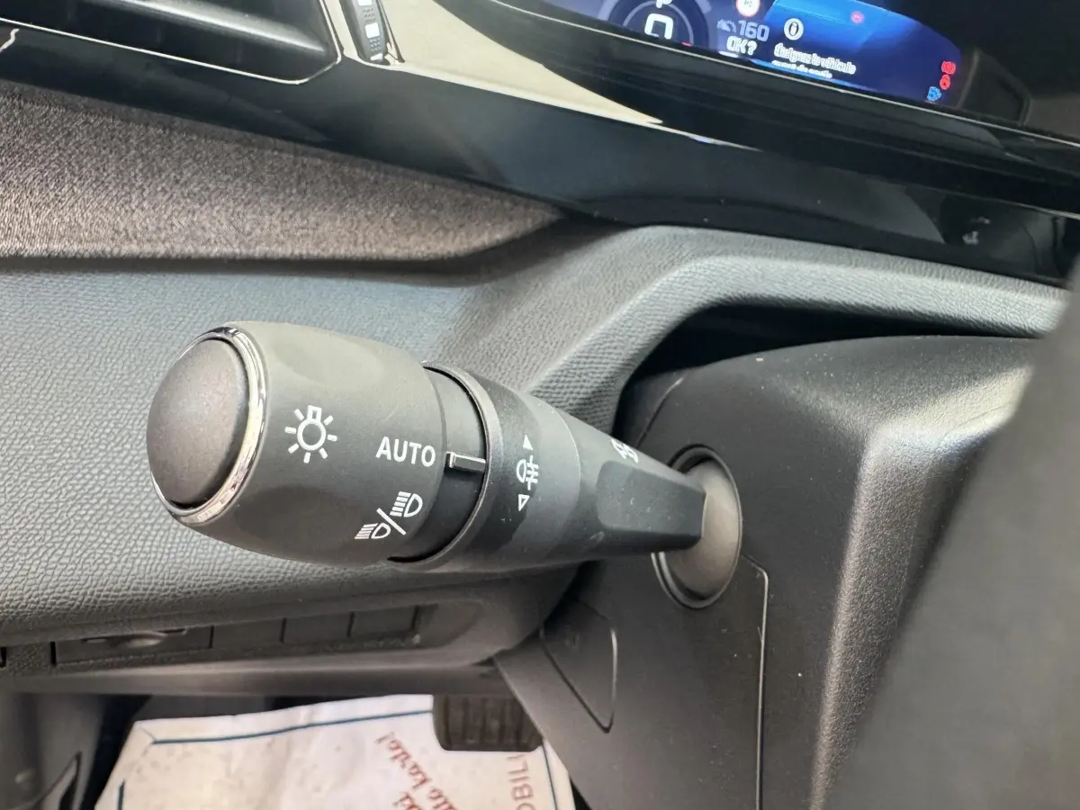 Gros plan sur la commande des phares avec réglage automatique dans l’habitacle gris d’une Peugeot 308 2026.