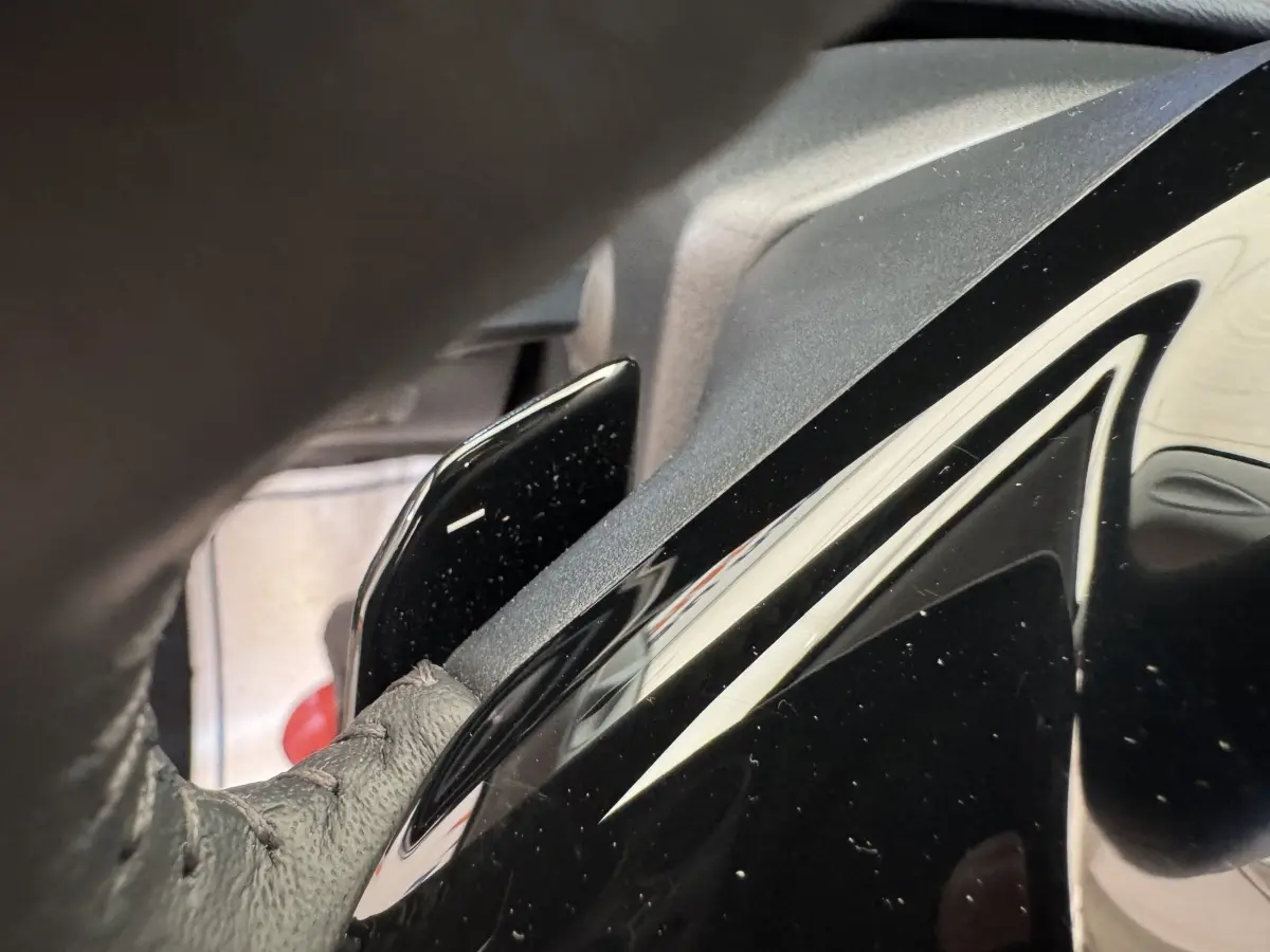 Gros plan sur le levier de palettes au volant cuir noir de la Peugeot 308 gris clair, intérieur côté conducteur.