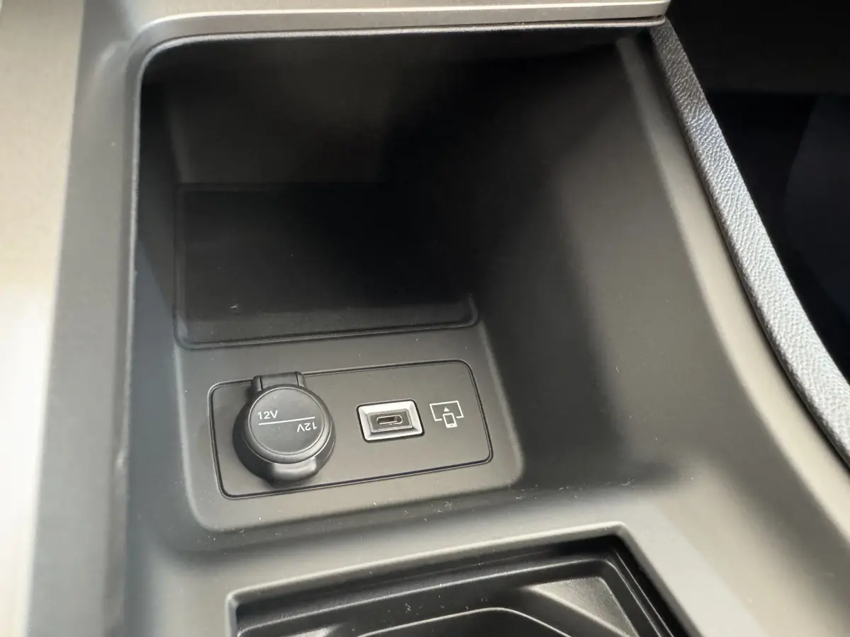 Gros plan sur la prise 12V et port USB dans le rangement central avant de la Peugeot 308 gris clair 2026.