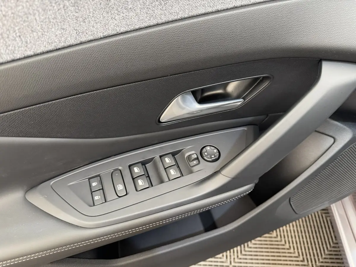 Vue rapprochée de la porte côté conducteur de la Peugeot 308 gris clair avec commandes électriques des vitres et rétroviseurs.