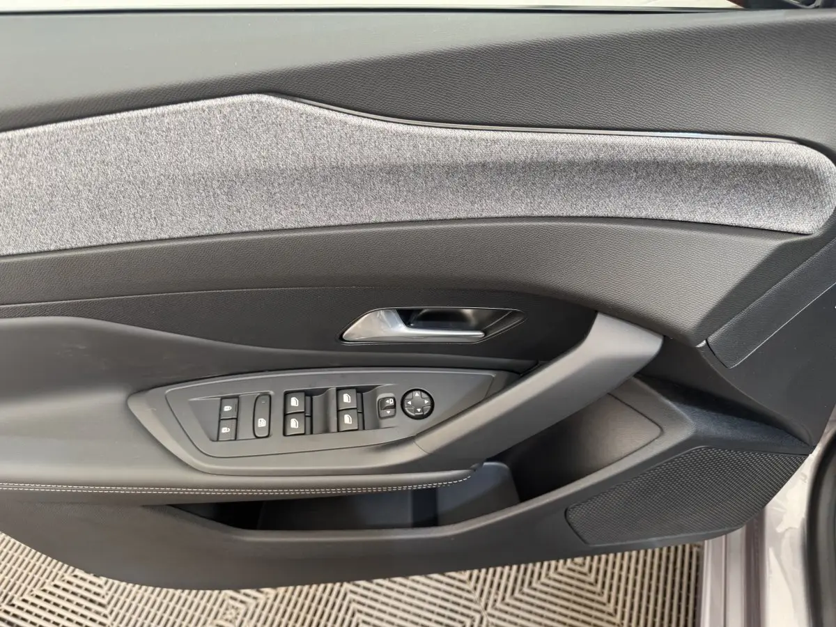 Vue rapprochée de la porte avant gauche de la Peugeot 308 gris clair, avec commandes électriques et habillage tissu gris.