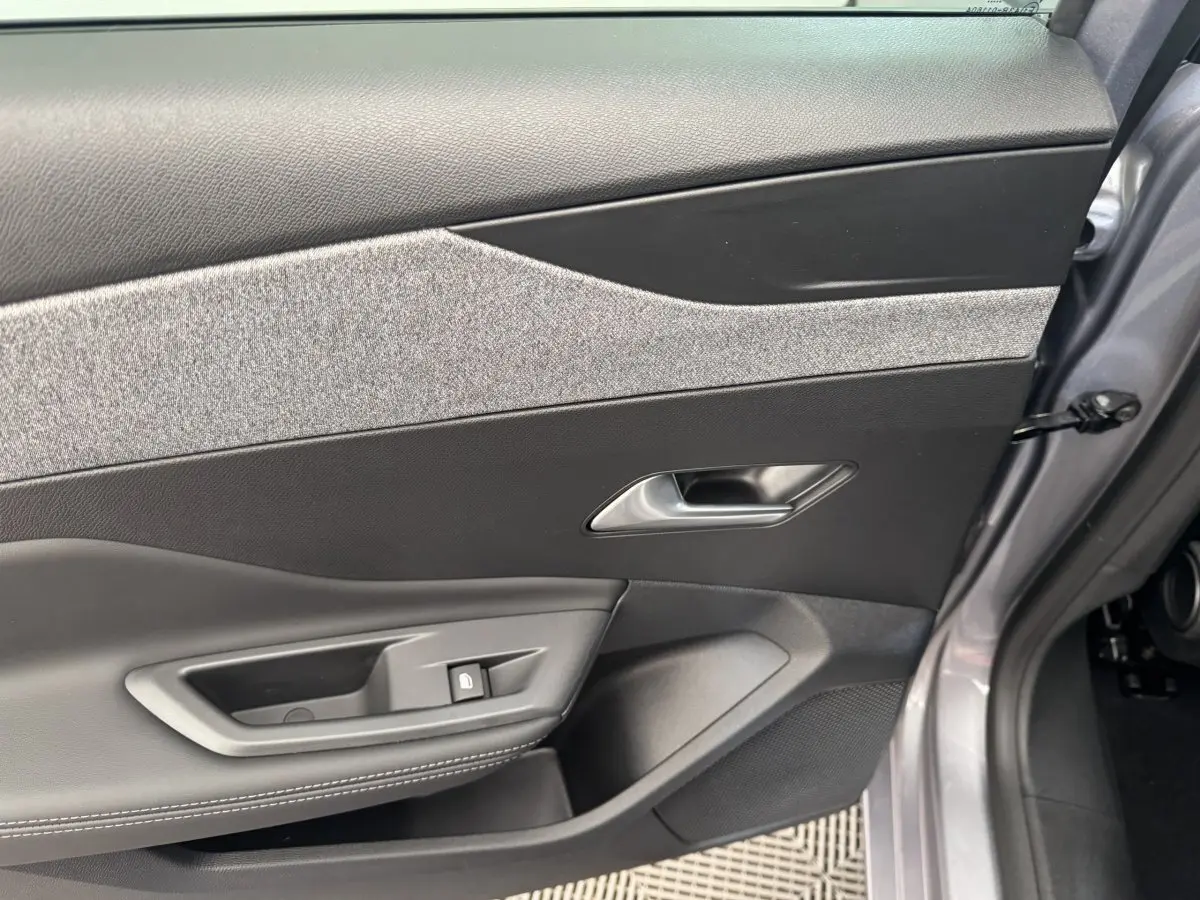 Vue intérieure côté gauche de la porte avant gris clair de la Peugeot 308 2026 avec garniture tissu et commandes électriques.