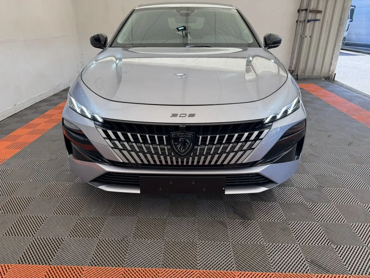 Vue frontale d'une Peugeot 308 gris clair 2026 avec calandre distinctive et phares LED fins allumés.