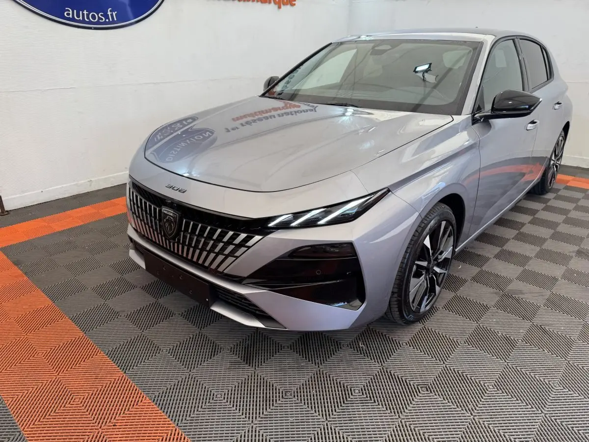 Peugeot 308 BlueHDi gris clair vue 3/4 avant droit, avec calandre distinctive et phares LED fins.