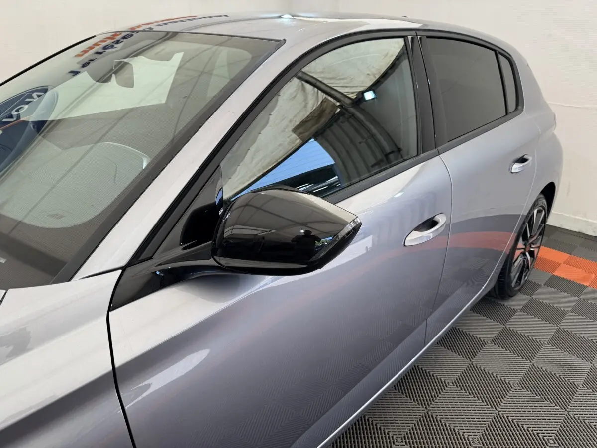 Vue latérale droite rapprochée d'une Peugeot 308 gris clair avec rétroviseur noir brillant et vitres teintées.