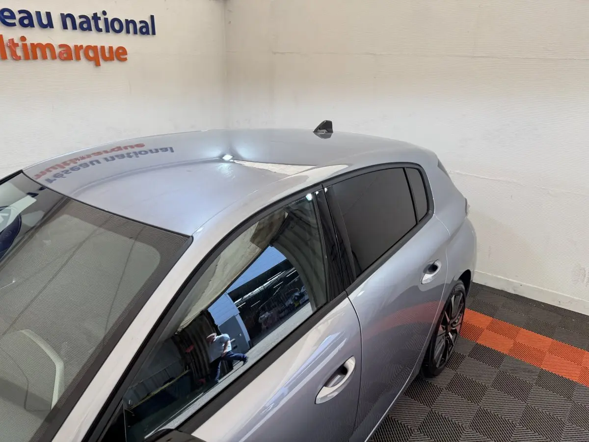 Vue 3/4 arrière droite d'une Peugeot 308 gris clair avec vitres teintées dans un showroom.