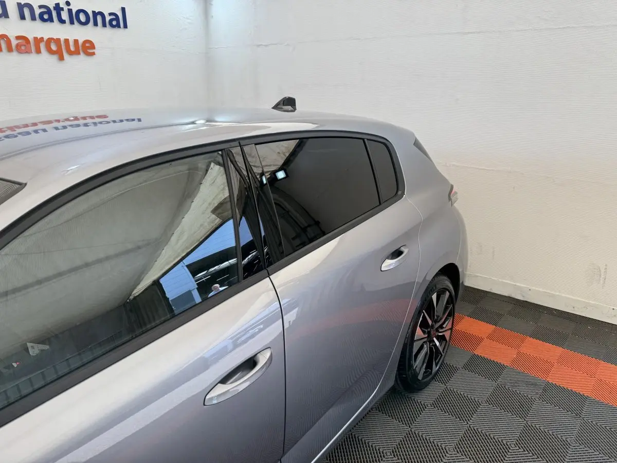 Vue 3/4 arrière côté droit d’une Peugeot 308 gris clair avec jantes alliage et vitres teintées dans un showroom.