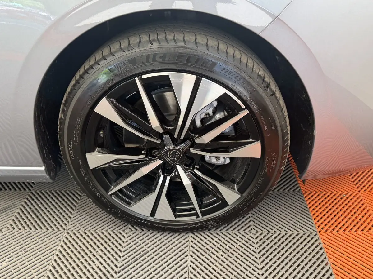Gros plan sur la roue avant droite d'une Peugeot 308 gris clair, jante alliage noire et argentée au design moderne.
