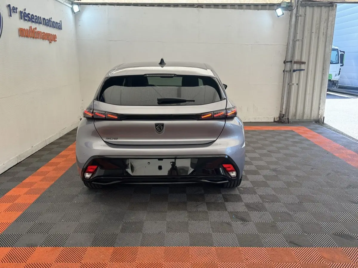 Vue arrière d'une Peugeot 308 gris clair 2026 avec feux LED et logo noir sur fond clair en intérieur showroom.